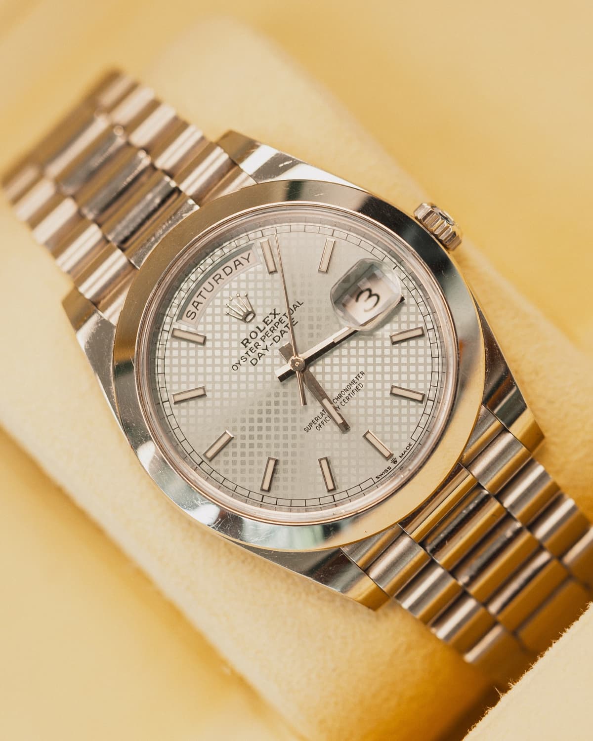 Silver Rolex Day-Date watch on cream backdrop