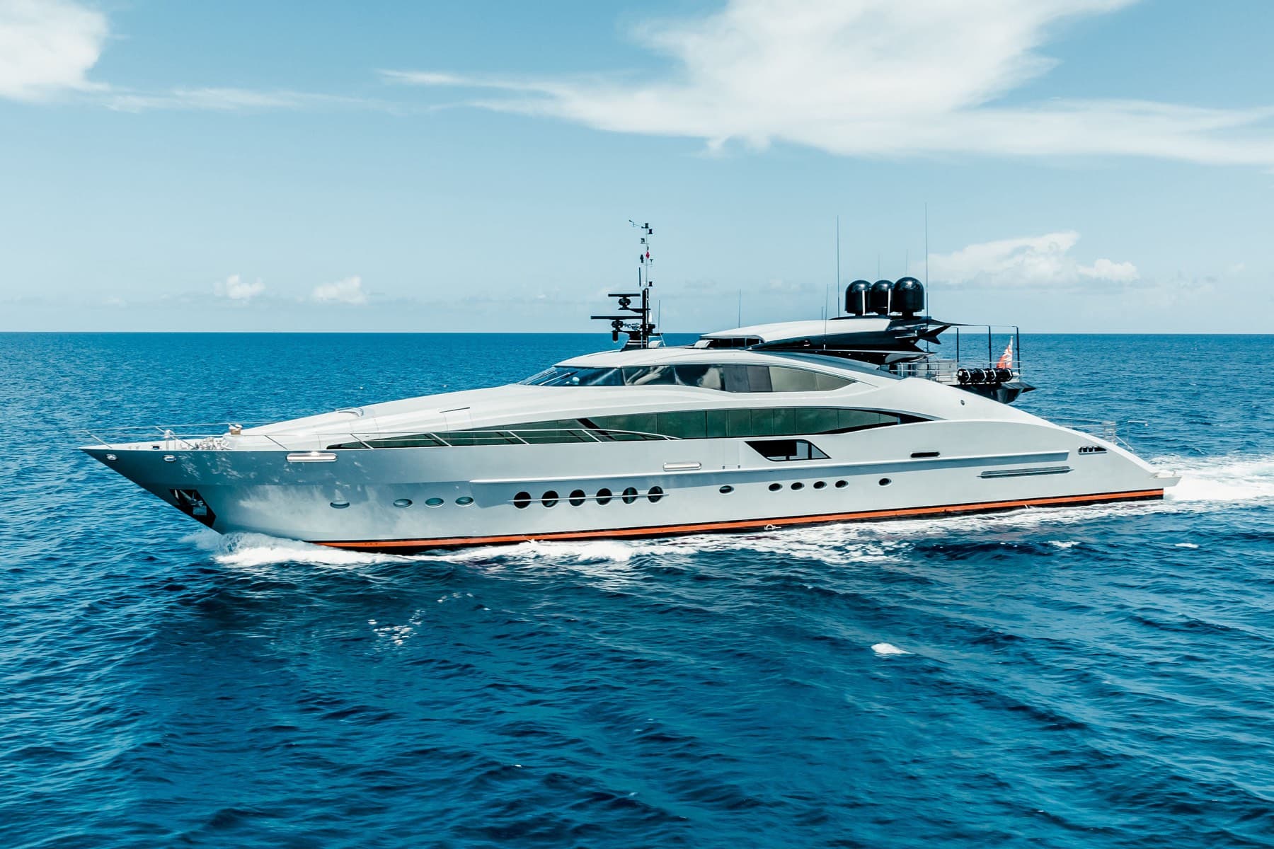 Sleek silver superyacht underway at speed across deep blue open water