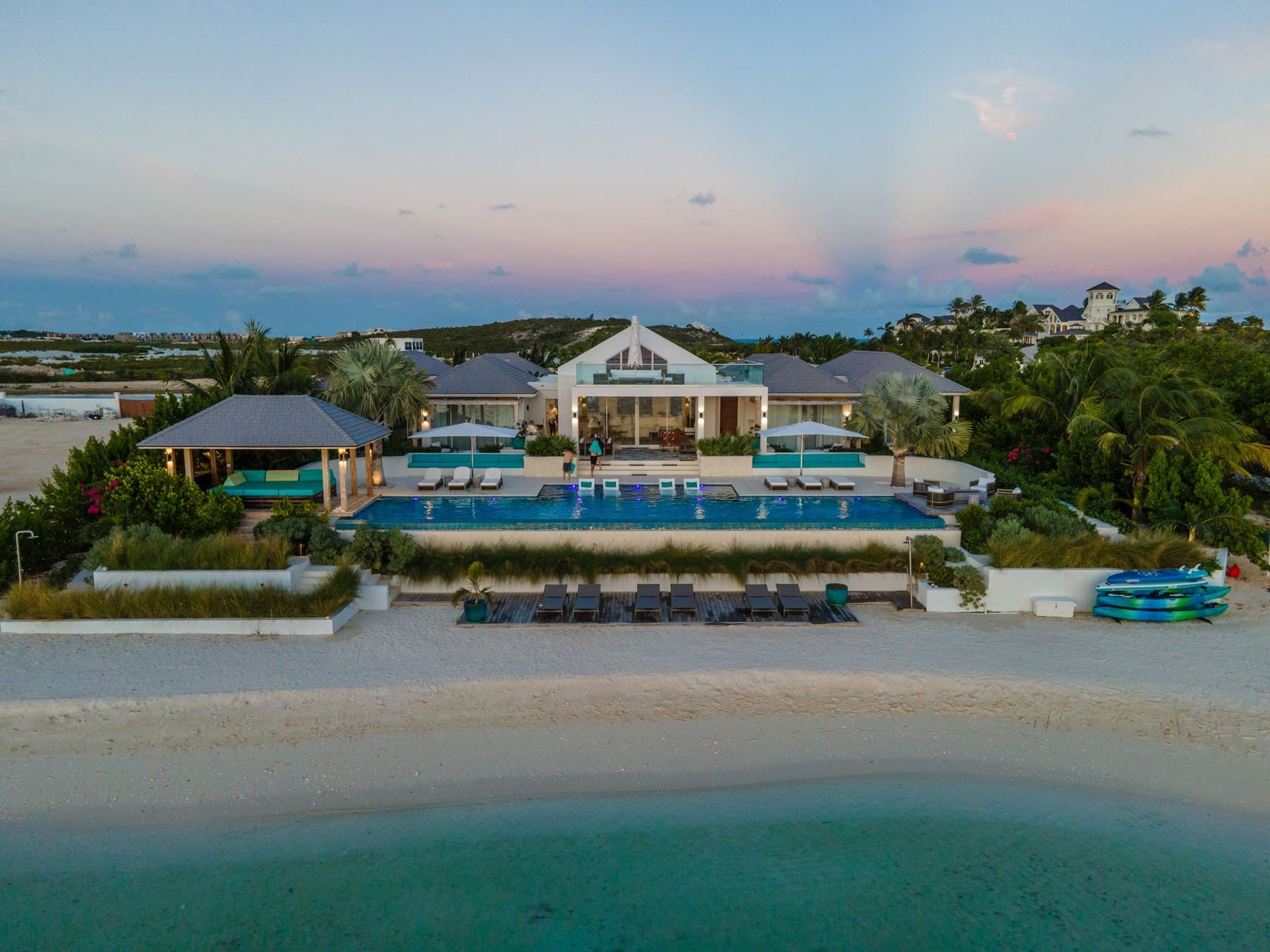 Sunset aerial from over turquoise water of beachfront villa and pool