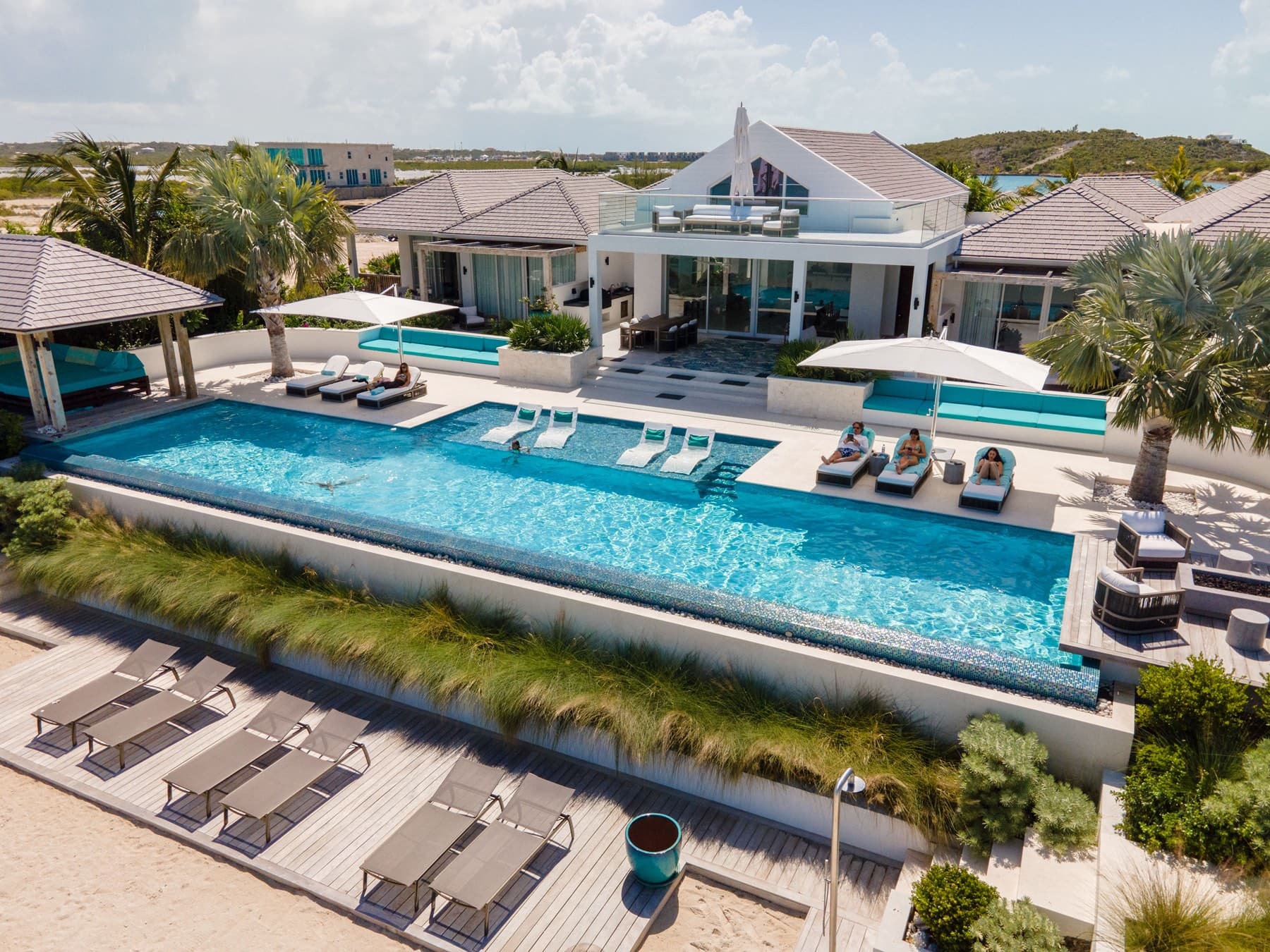 Aerial of infinity pool deck, umbrellas, and guests at beachfront villa