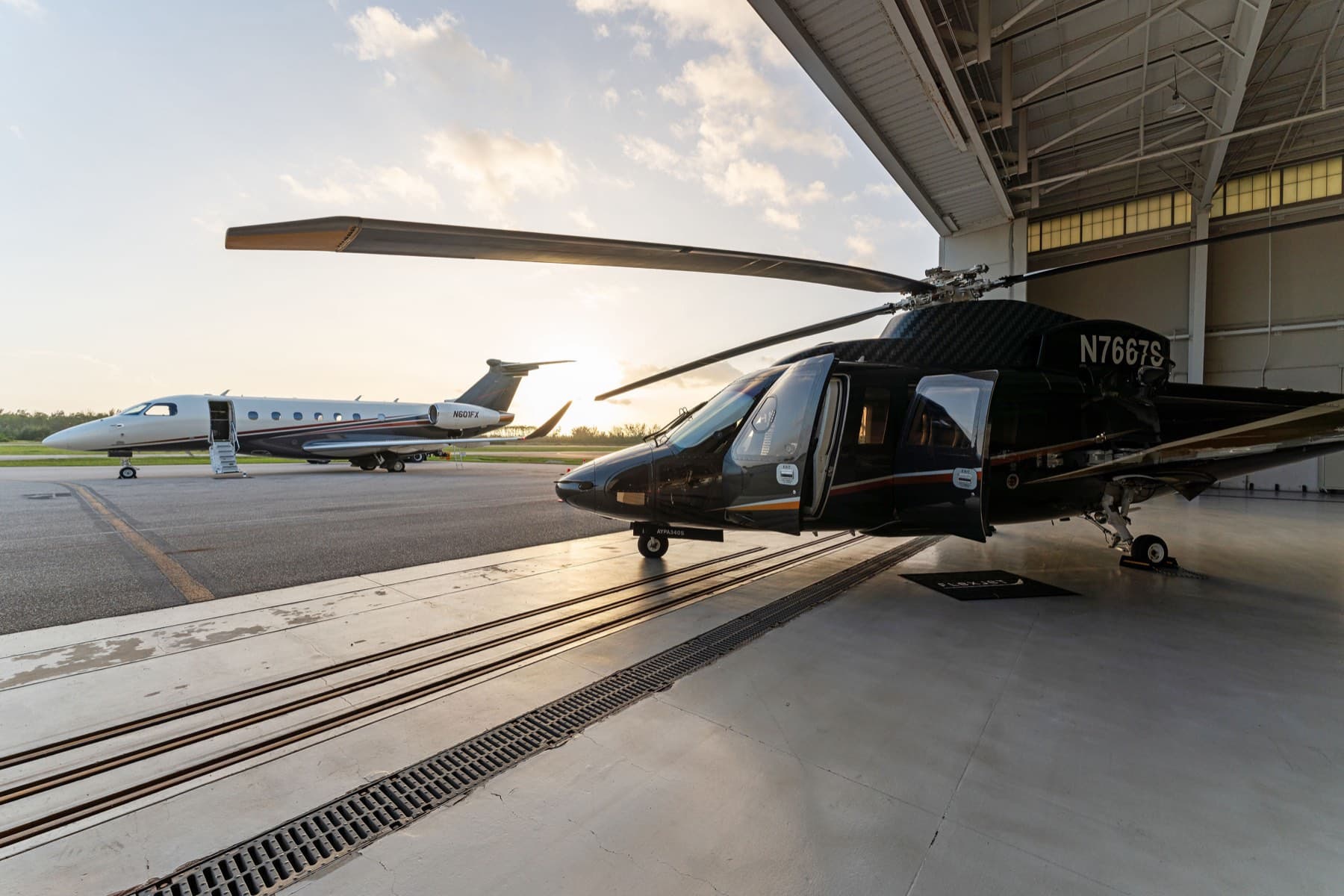 Sikorsky helicopter and private jet on hangar ramp at golden hour