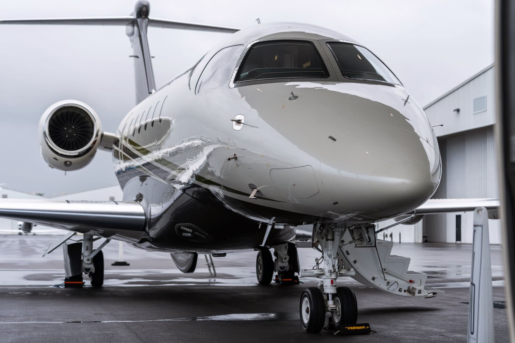 Front three-quarter view of polished private jet nose on wet tarmac