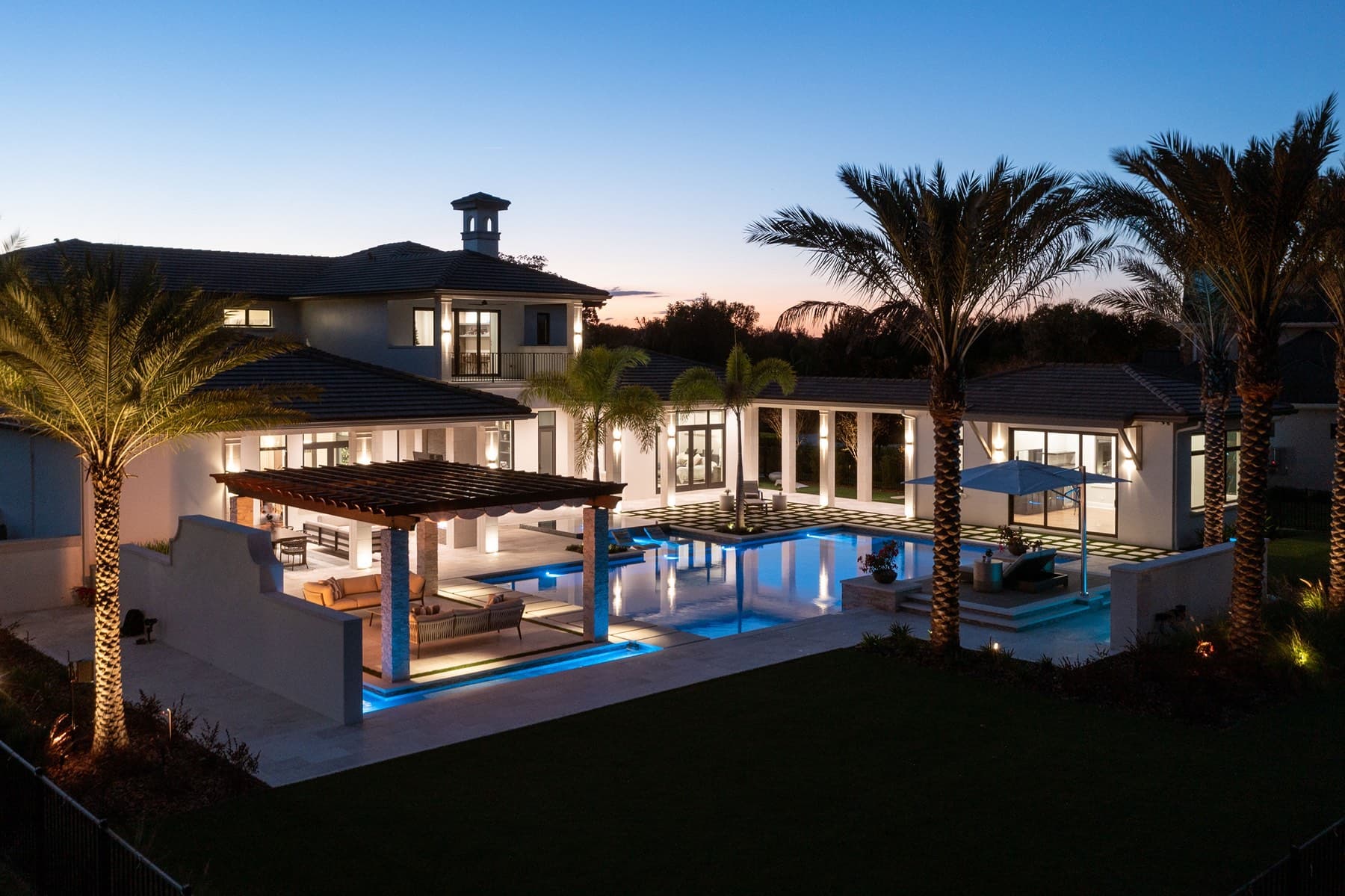 Twilight aerial of estate rear with pergola, pool, and palm-framed terrace