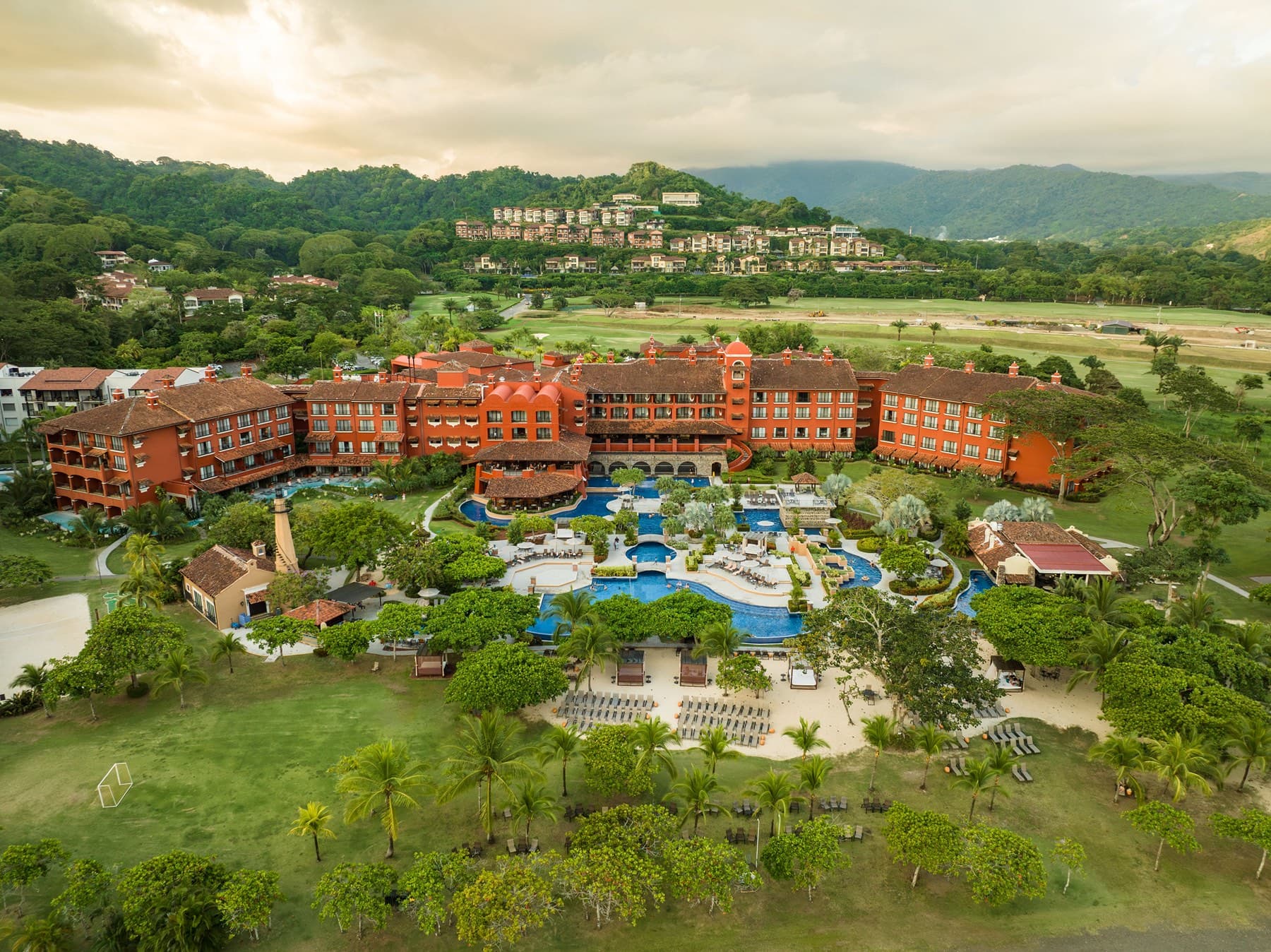 Aerial view of terracotta resort hotel and pools against rainforest mountains