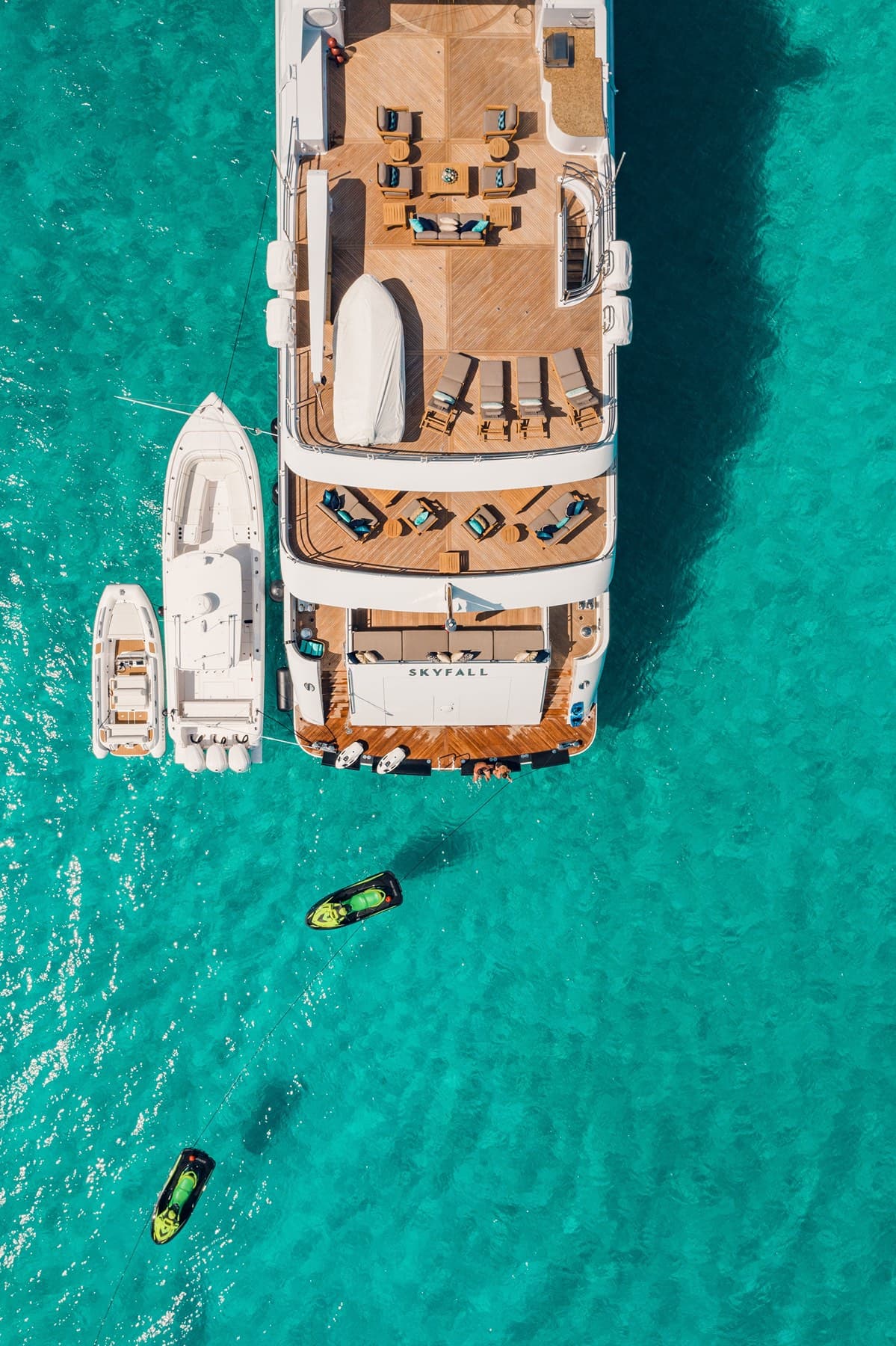 Top-down aerial of superyacht with tenders over gin-clear turquoise flats