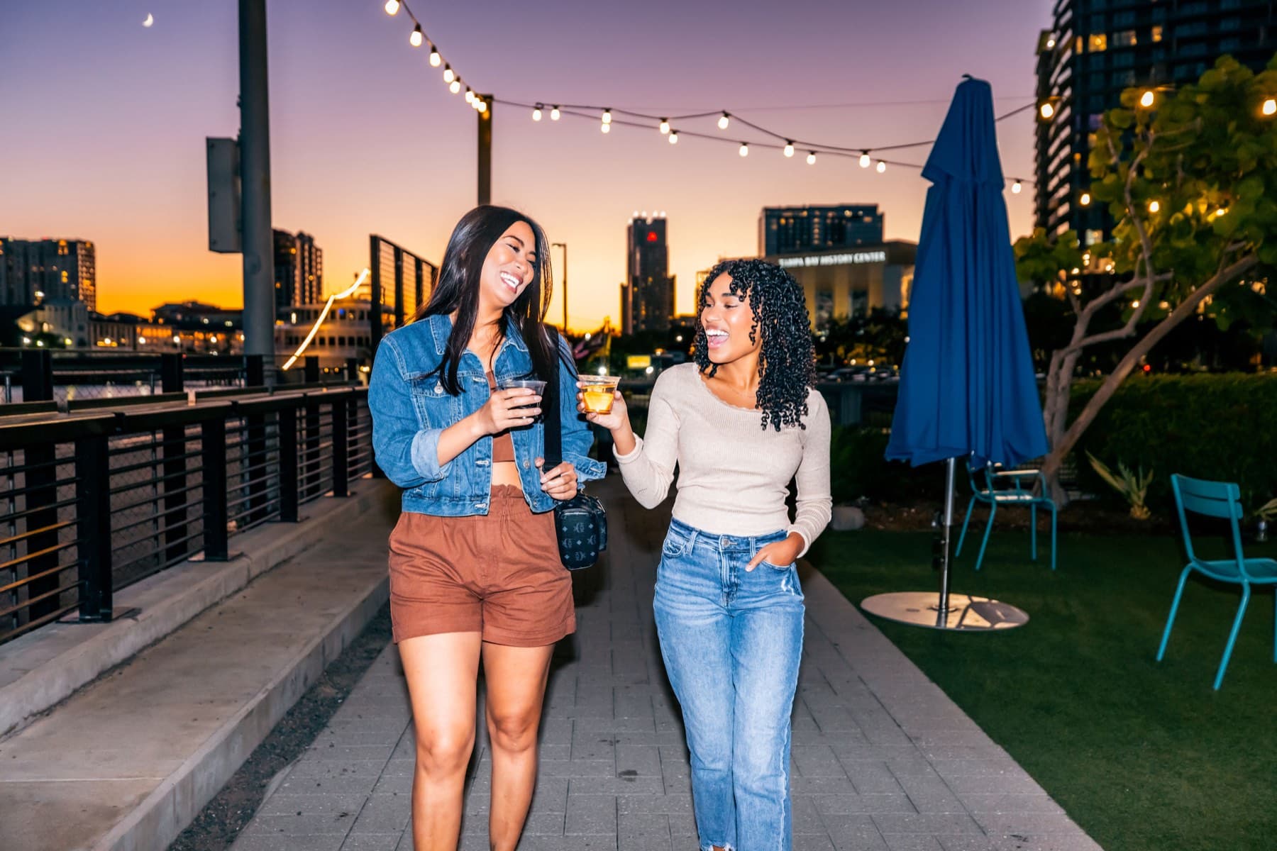 Two friends with drinks strolling the waterfront at vivid sunset
