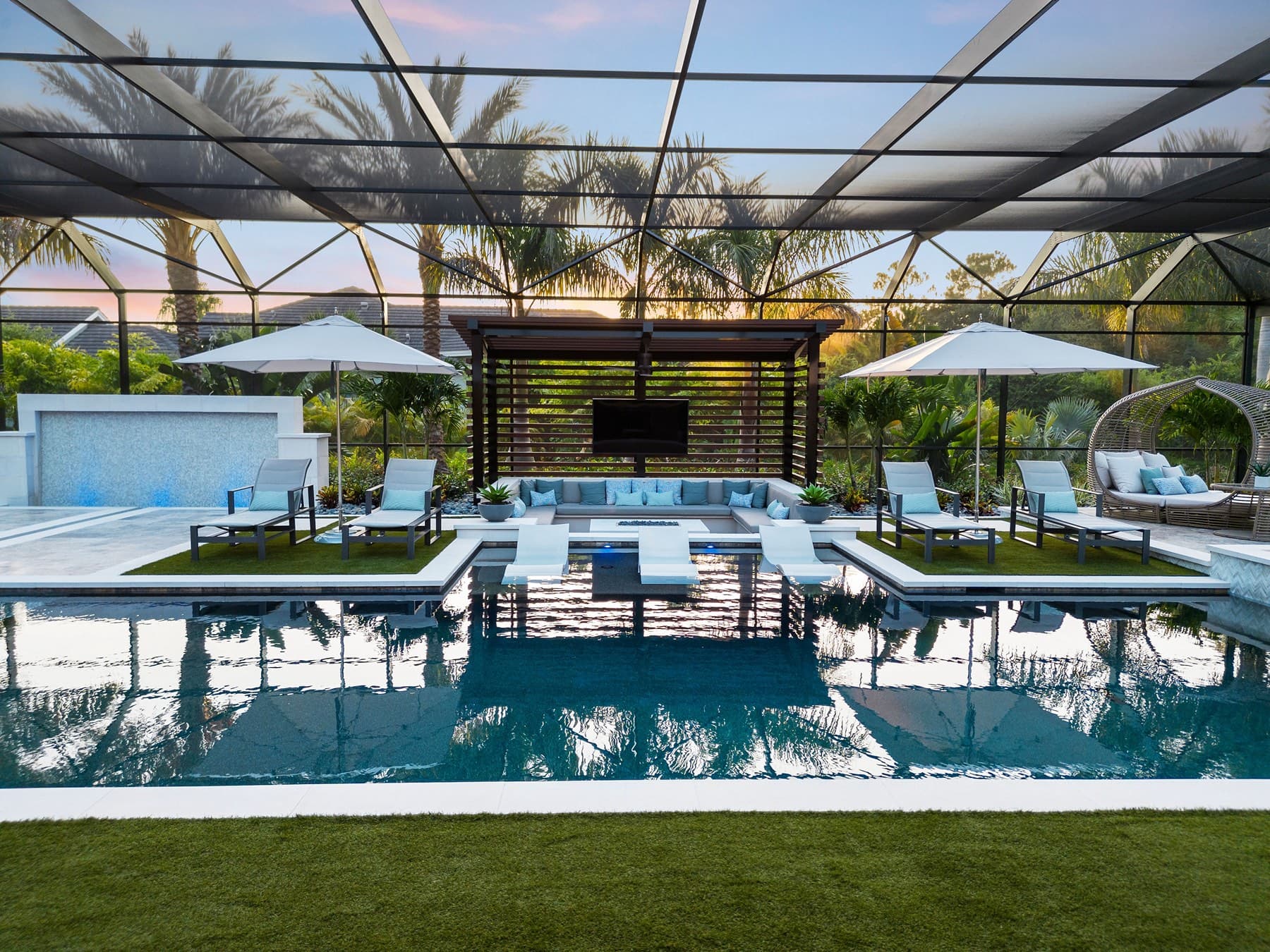 Sunset view of symmetrical screened pool terrace with cabana and umbrellas